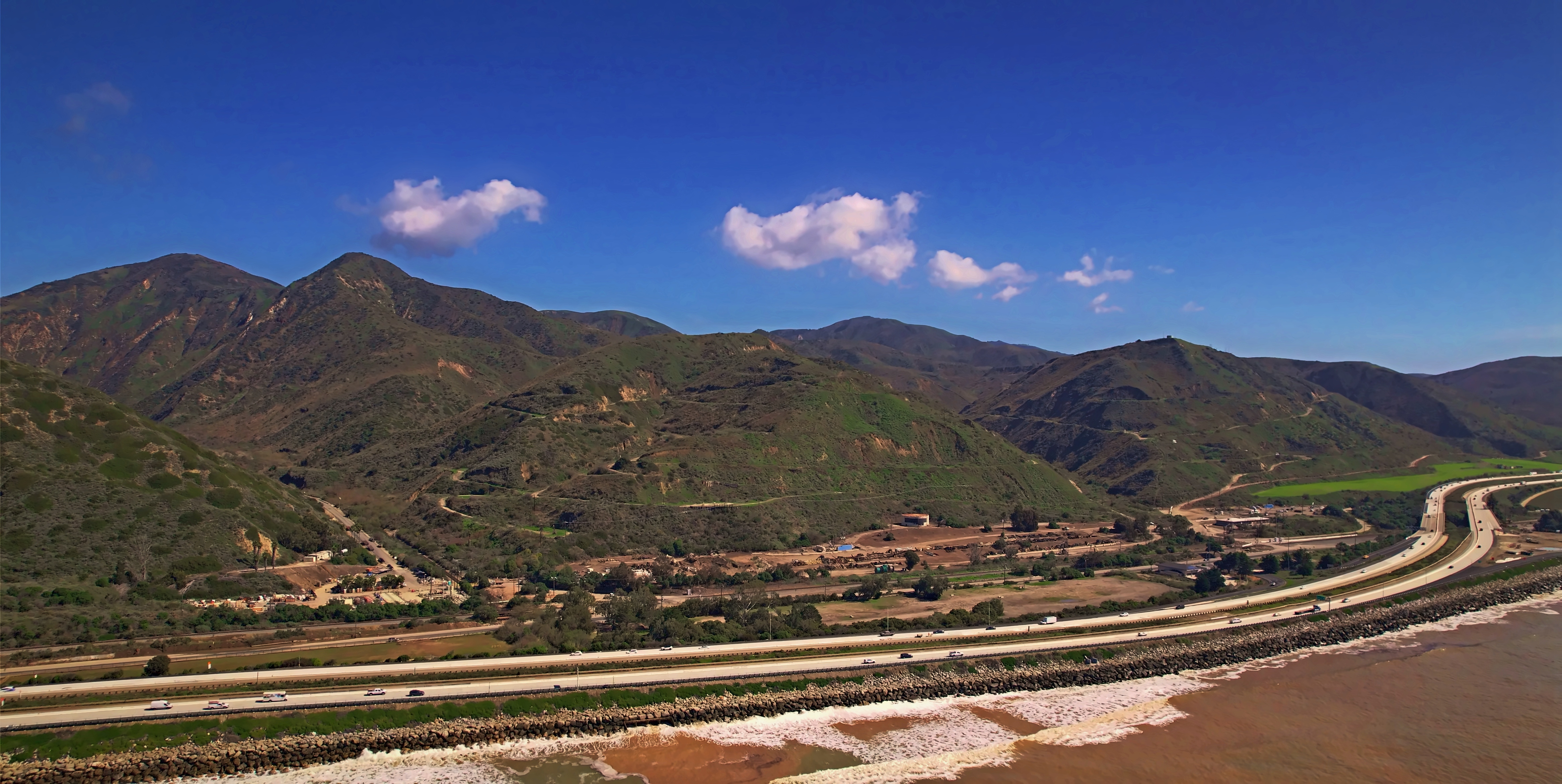 SKYSPECS Digital coastal landscape photograph showing a highway along mountains and Pacific shoreline