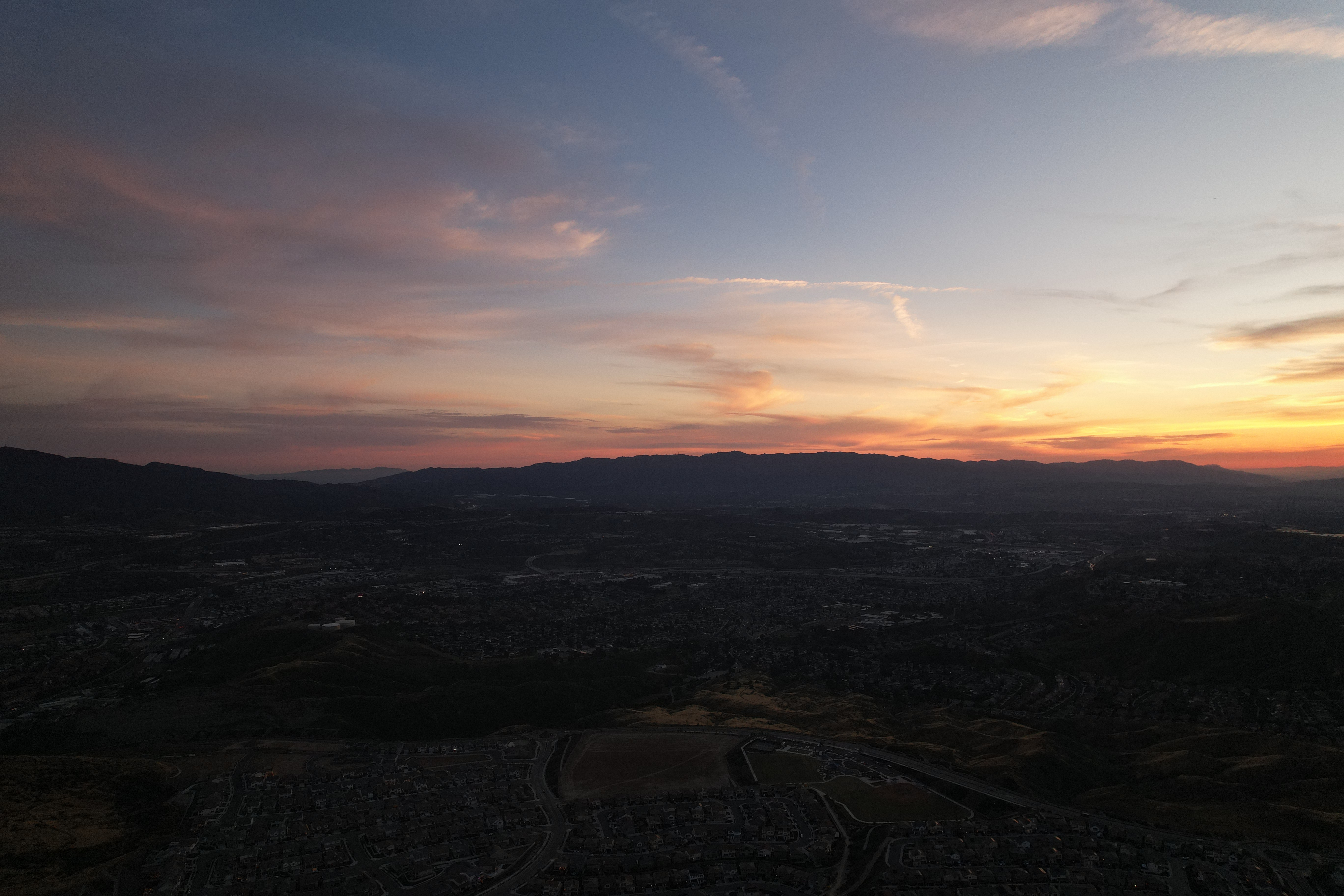 SKYSPECS Digital aerial cityscape photograph showing a Southern California valley at sunset with mountain silhouette and cinematic sky